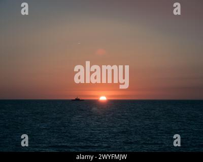 Una nave militare della Marina spagnola che naviga all'orizzonte durante il tramonto, a Cadice, in Andalusia, in Spagna Foto Stock