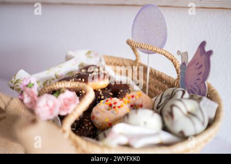Dettaglio di un cestino con mini ciambelle di colore pasquale su un tavolo di caramelle pasquali. Dolci tipici di Pasqua su un tavolo festivo con uova di Pasqua, ch Foto Stock
