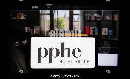 Persona che detiene un cellulare con il logo della società di ospitalità britannica PPHE Hotel Group Limited di fronte alla pagina web aziendale. Mettere a fuoco il display del telefono. Foto Stock