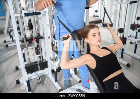 Donna che fa esercizi sulla macchina sotto la supervisione di un fisioterapista Foto Stock