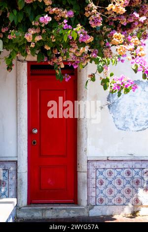 Una porta rossa nella città vecchia di Lisbona con Azulejos e alberi in fiore, Portogallo Foto Stock