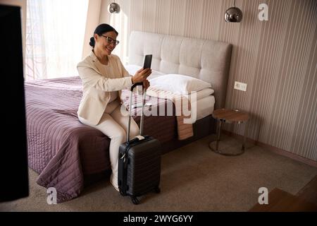 Bella donna che fa videochiamata sullo smartphone nella sua suite Foto Stock