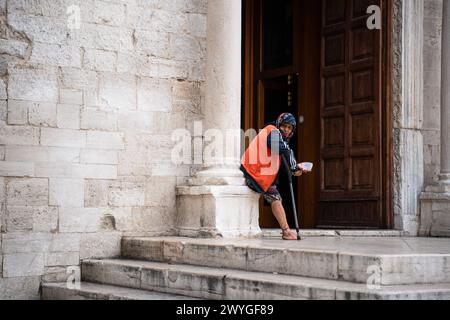 Bari, Italia - 22 settembre 2023: Un'anziana donna in stampelle chiede soldi davanti ad una chiesa di Bari, Italia *** Eine alte Frau auf Krücken bettelt vor einer Kirche di Bari, Italien um Geld Foto Stock