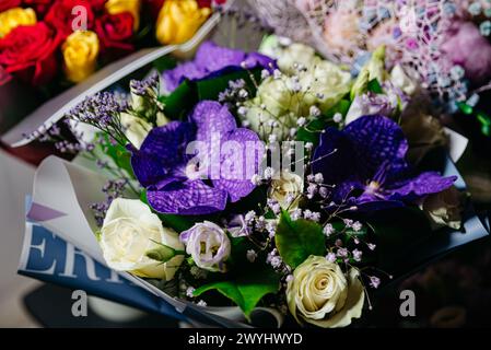 Bouquet vibrante caratterizzato da splendide orchidee viola, delicate rose bianche e morbidi accenti lavanda, avvolto in un elegante foglio di carta. Foto Stock