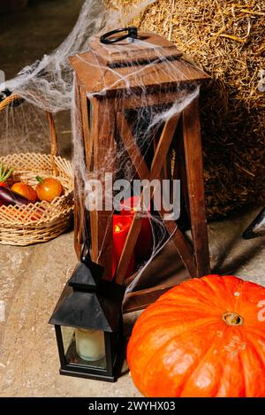 Spaventoso ambiente di Halloween con una grande zucca, ragnatele, una lanterna rustica e una balla di fieno, perfetta per l'arredamento stagionale. Foto Stock