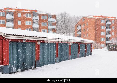 Una fila di edifici residenziali rossi e blu a Mölndal, in Svezia, coperti da una coperta di neve. In primo piano, c'è un garage con nevicate Foto Stock