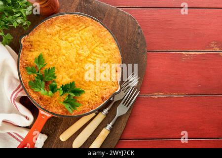 Shepherd's Pie con manzo macinato, piselli, carote, cipolle, patate e formaggio su vecchio fondo in legno in padella di ghisa. Tradizionale piatto inglese fatto in casa Foto Stock