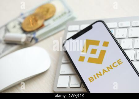 KIEV, UCRAINA - 15 MARZO 2024 Logo Binance sullo schermo dell'iPhone su tastiera bianca con denaro e bitcoin. Portale di scambio di criptovalute Foto Stock