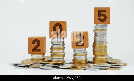 Cubi di legno su una pila di monete con la parola 2025. Concetto di tasse, piano di bilancio finanziario, investimenti, risparmi e risoluzioni di Capodanno Foto Stock