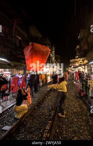 Turisti e curiosi partecipano all'uscita serale di lanterne per augurare il nuovo anno sui binari del treno di Shifen Foto Stock