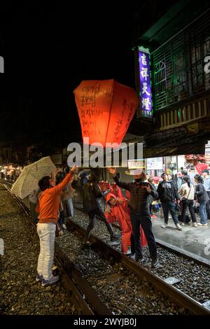 Turisti e curiosi partecipano all'uscita serale di lanterne per augurare il nuovo anno sui binari del treno di Shifen Foto Stock