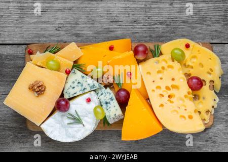 Assortimento di formaggi su tagliere in legno. Piatto di formaggi servito con uva, melograno e rosmarino, vari formaggi su un piatto. vista dall'alto Foto Stock