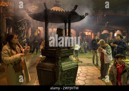 Devoti che pregano nel tempio Baoan pieno di fumo di incenso, durante una cerimonia di Capodanno cinese Foto Stock