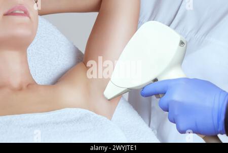 Il cosmetologo esegue la procedura di epilazione laser nella zona delle ascelle, a una giovane donna in un salone di bellezza. Foto Stock