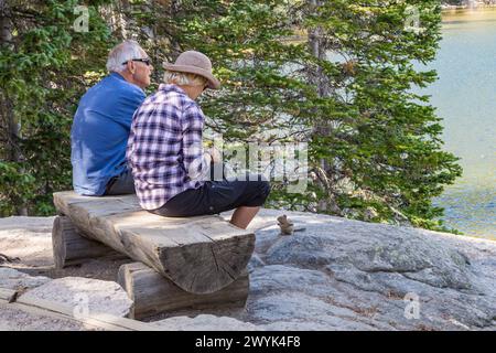 Coppia seduta sulla panchina che dà da mangiare ai chipmonaci lungo il Bear Lake Nature Trail nel Rocky Mountain National Park, Colorado Foto Stock