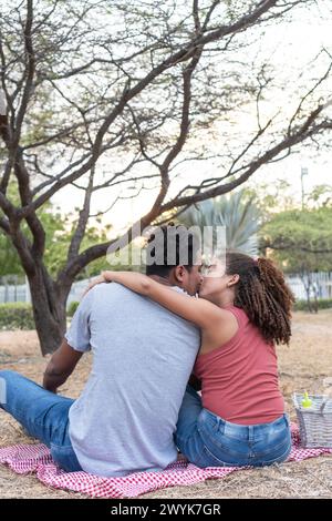 Un bacio romantico condiviso tra una coppia al tramonto, incorniciato da alberi. Foto Stock