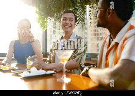 Un giovane sorridente che parla con gli amici nel pub sul tetto Foto Stock