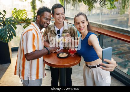 Una giovane donna sorridente che si fa selfie con gli amici quando si trovano al bar sul tetto Foto Stock