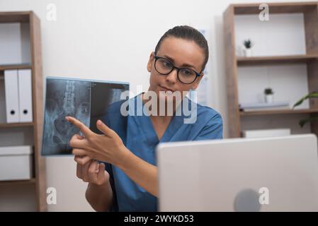 medico che indica la pellicola radiografica che mostra al paziente nel computer portatile durante la consultazione online di telemedicina Foto Stock