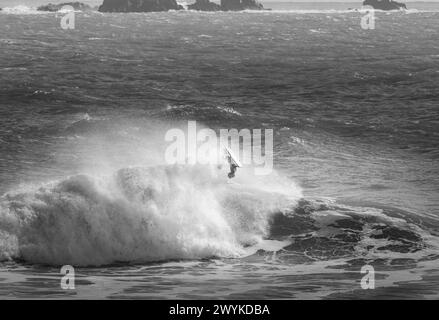 Wave board o body board navigando in enormi breakers a Kynance Cove, Cornovaglia. Esecuzione di un ribaltamento acrobatico. Affrontare le onde. Immagine monocromatica. Foto Stock