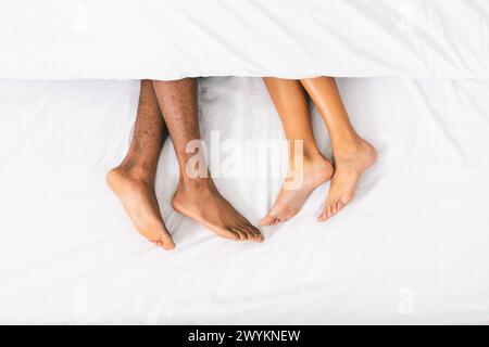 Amate le gambe di coppia sdraiate sul letto sotto la coperta Foto Stock