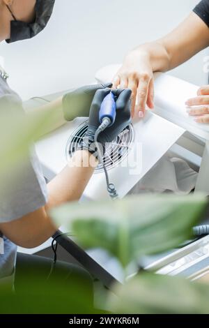 Master femmina che usa la lima elettrica del chiodo mentre fa manicure per cliente in salone di bellezza Foto Stock