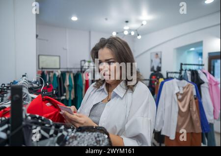 Una donna grassa guarda con orrore al prezzo di un abito in un negozio Plus size. Foto Stock