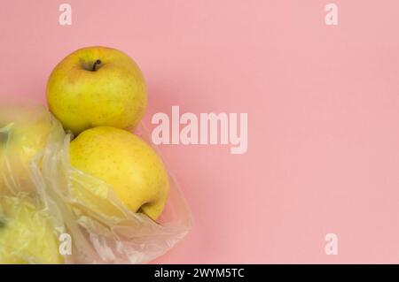 Tre mele in un sacchetto di plastica su sfondo rosa. Le mele sono gialle e lucide Foto Stock