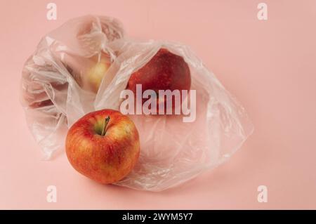 Tre mele sono in sacchetti di plastica su sfondo rosa. Le mele sono rosse e lucide. I sacchetti sono trasparenti e trasparenti Foto Stock