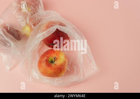 Un sacchetto di plastica con una mela rossa all'interno. Il sacchetto è posizionato su uno sfondo rosa. Concetto di spreco e preoccupazione ambientale, come il sacchetto di plastica i Foto Stock