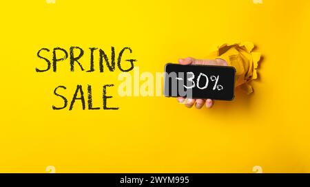 Una persona che ha un cellulare con le parole "Spring sale" scritte sopra. Il telefono viene tenuto in alto per rivelare un segno nero con le parole 30 spente Foto Stock