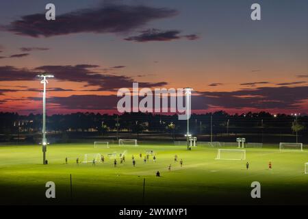 Arena sportiva pubblica illuminata a North Port, Florida, con persone che giocano una partita di calcio sullo stadio di calcio in erba al tramonto. Concetto di attività all'aperto Foto Stock