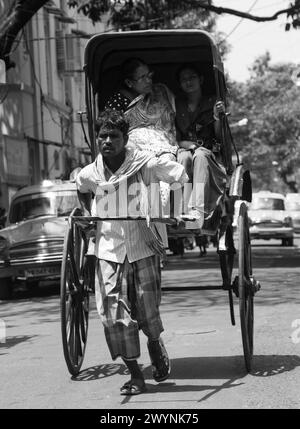 Wallah di risciò di Kolkata con passeggeri. Kolkata è tra gli unici luoghi al mondo in cui flotte di risciò tirati a mano continuano a girovagare per le strade. Foto Stock