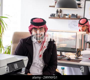 In un elegante ambiente d'ufficio, un gentiluomo arabo siede comodamente sulla sua sedia, trasudando fiducia e calore. Con un sorriso genuino che abbellisce il suo volto, Foto Stock