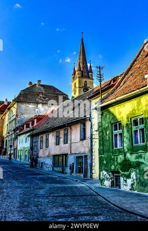 Case con occhi che fiancheggiano strada Ocnei e la cima della torre dell'orologio della cattedrale evangelica di Santa Maria a Sibiu, Transilvania, Romania Foto Stock