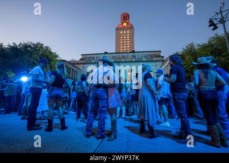 Austin Texas USA, 5 aprile 2024: La University of Texas Tower, illuminata in arancione, incombe sul palco e sul pubblico del campus durante un'esibizione registrata da star della musica country. L'evento si è tenuto per promuovere il prossimo spettacolo Country Music Television (CMT) Awards presso l'arena Moody Center di Austin. ©Bob Daemmrich Foto Stock