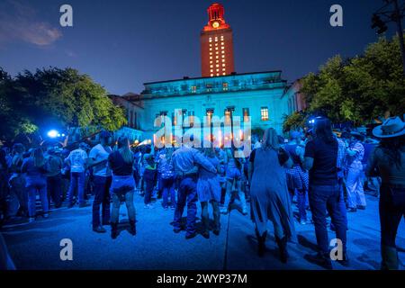 Austin Texas USA, 5 aprile 2024: La University of Texas Tower, illuminata in arancione, incombe sul palco e sul pubblico del campus durante un'esibizione registrata da star della musica country. L'evento si è tenuto per promuovere il prossimo spettacolo Country Music Television (CMT) Awards presso l'arena Moody Center di Austin. ©Bob Daemmrich Foto Stock