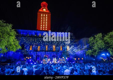 Austin Texas USA, 5 aprile 2024: La University of Texas Tower, illuminata in arancione, incombe sul palco e sul pubblico del campus durante un'esibizione registrata da star della musica country. L'evento si è tenuto per promuovere il prossimo spettacolo Country Music Television (CMT) Awards presso l'arena Moody Center di Austin. ©Bob Daemmrich Foto Stock