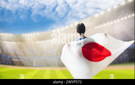 Tifoso di calcio giapponese nello stadio. Tifosi giapponesi sul campo da calcio che guardano le partite di squadra. Gruppo di tifosi con bandiera e maglia nazionale che tira Foto Stock