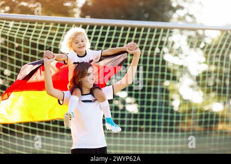 I bambini giocano a football all'aperto. Tifosi della Germania con bandiera nazionale. I bambini segnano un gol alla partita di calcio. Bambino in maglia tedesca Foto Stock