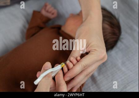 La mamma taglia le unghie del figlio appena nato con le forbici per bambini piccoli. Foto Stock