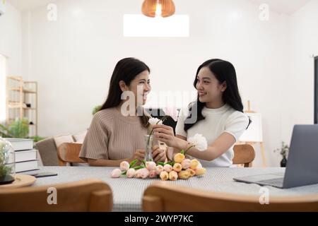 Madre anziana e figlia adulta felici sul tavolo mentre sistemano i fiori in un vaso insieme. Tecnologia e stile di vita. Buon tempo insieme Foto Stock