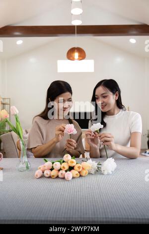 Madre anziana e figlia adulta felici sul tavolo mentre sistemano i fiori in un vaso insieme. Tecnologia e stile di vita. Buon tempo insieme Foto Stock