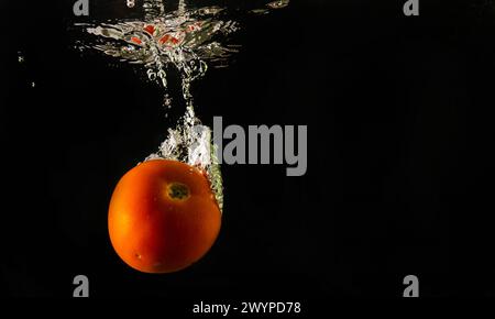 Pomodoro maturo cade profondamente sotto l'acqua con un grande splash. Foto Stock