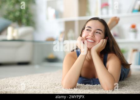 Donna felice che sogna di guardare sopra sdraiata su un tappeto a casa Foto Stock