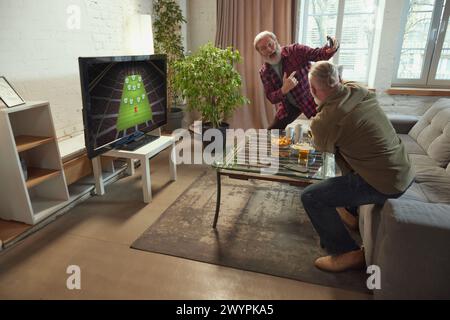 Due uomini estremamente emotivi, anziani che guardano a casa la traduzione online delle partite di calcio, urlano, esprimono felicità. Partita vincente Foto Stock
