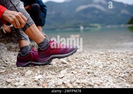 Primo piano di una donna attiva che indossa scarponi da trekking sulla riva del lago di montagna. Turisti anziani che amano la natura all'inizio della primavera. Foto Stock