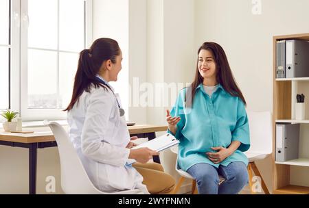 Sorridente donna incinta felice che visita il suo medico ostetrico in clinica di maternità. Foto Stock