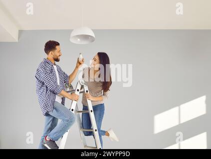 Allegra giovane coppia che cambia lampadina in appartamento Foto Stock