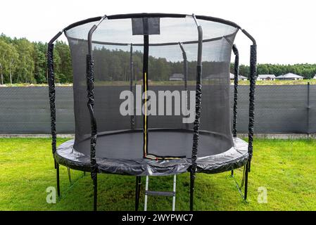 Trampolino per bambini di grandi dimensioni con rete protettiva e cerniera chiusa, in piedi in giardino, rete a vista che maschera la recinzione. Foto Stock